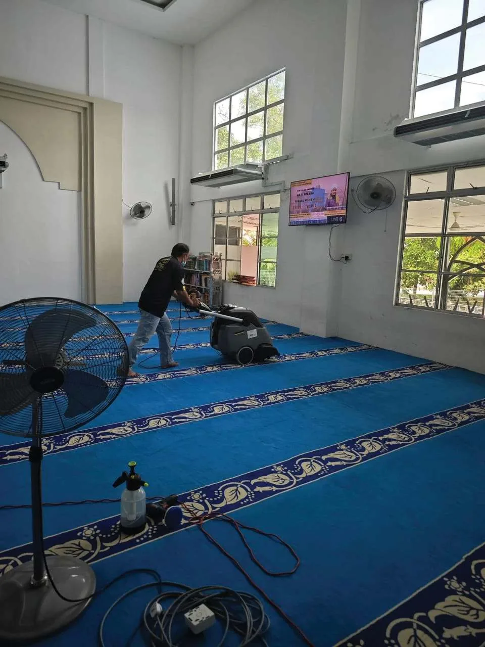 Pekerja mencuci karpet biru dewan solat masjid menggunakan mesin ekstraksi Kärcher